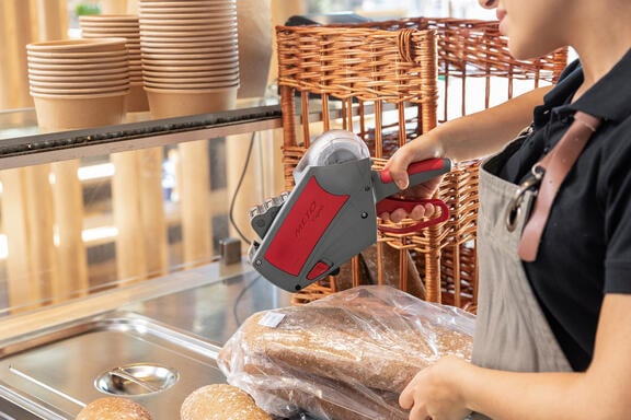 Meto Expert price labeler in gray and red labeling fresh baked goods in a bakery